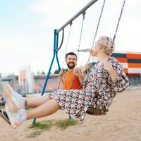 Romantic couple is having fun outside. Enjoying spending time together on a swings.