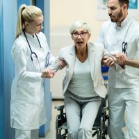 Disabled female patient looking surprised while getting up form the wheelchair with help of two doctors in the hospital.